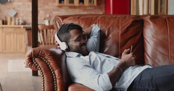Chlápek ve sluchátkách relaxovat na pohovce poslouchat hudbu používat mobil — Stock video
