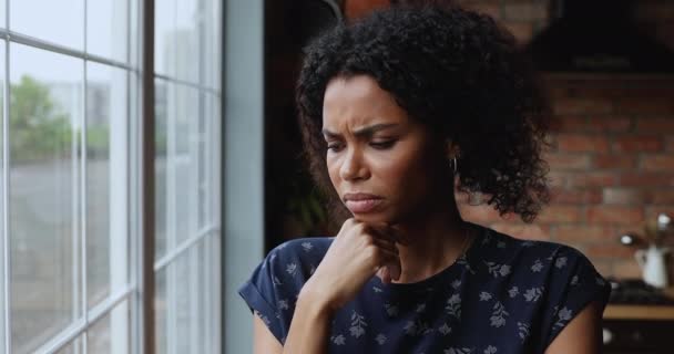 Депрессивная африканская женщина думает о проблемах, глядя в окно — стоковое видео