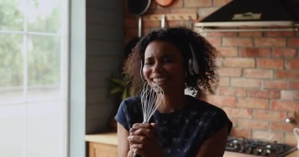 Mujer africana en auriculares sostiene batidor cantar canción en la cocina — Vídeo de stock