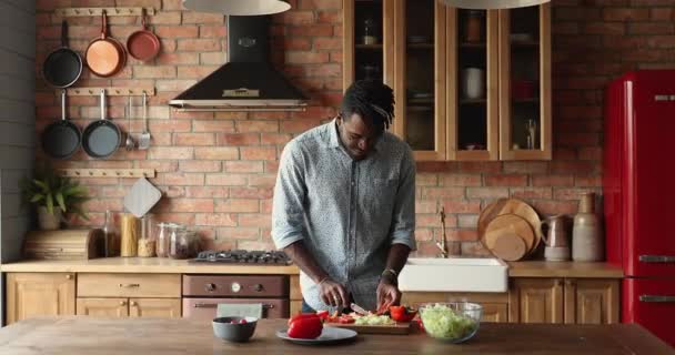 Yakışıklı Afrikalı adam mutfakta salata pişirirken müzik dinliyor. — Stok video