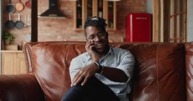 Afrikalı adam kanepeye oturur, akıllı telefonu tutar ve telefonla konuşur.