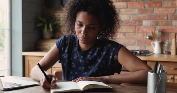 Mujer africana enfocada sentada a la mesa escribiendo en un diario personal — Vídeos de Stock
