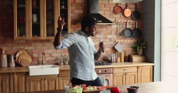 Африканський хлопець тримає бітер, наче мікрофон, який танцює на кухні. — стокове відео