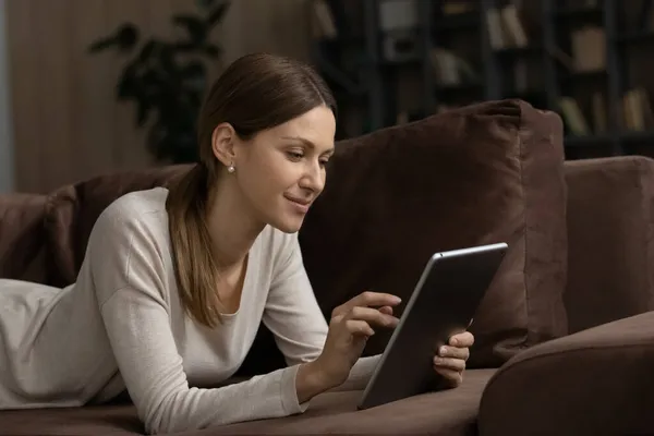 Lachende aantrekkelijke vrouw ontspannen alleen op de bank met digitale tablet — Stockfoto