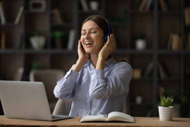 Huzurlu bir kadın masasına oturmuş kulaklık takıyor ve müziğin tadını çıkarıyor.