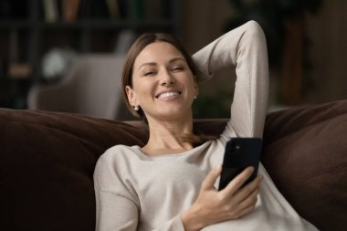 Kanepede dinlenen kadın akıllı telefon tebessümü tutuyor. Kameraya bak.