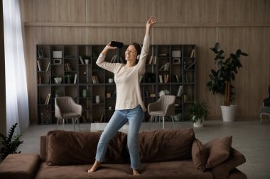 Kanepede dans eden kadın akıllı telefonuyla kulaklıkla müzik dinliyor.