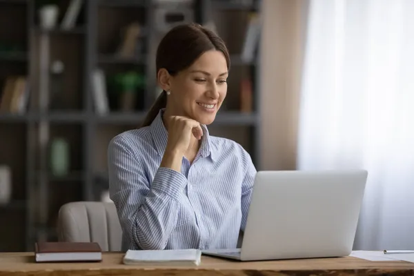 Aantrekkelijke glimlachende zakenvrouw zitten op de werkplek werken aan laptop — Stockfoto