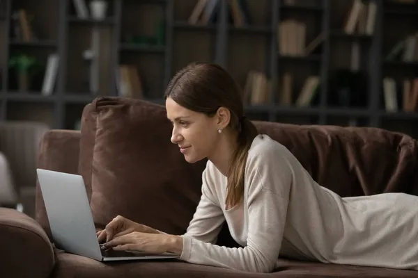 Žena ležící na gauči v obývacím pokoji pracuje na notebooku — Stock fotografie