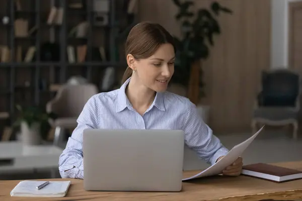 Affärskvinna sitter vid skrivbordet med bärbara datorer innehav papper läsa dokument — Stockfoto