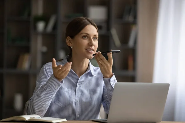 Mujer atractiva sentarse en el escritorio celebración de teléfono inteligente hablar en speakerphone — Foto de Stock