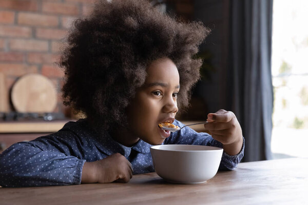 Happy hungry little African American kid eating fast breakfast.