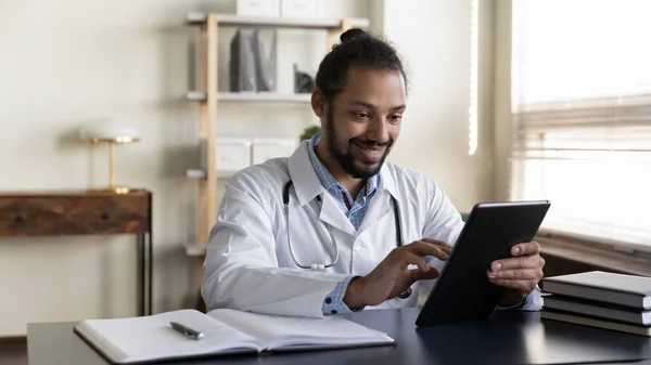 Sonriente hombre afroamericano médico usando tableta en el consultorio —  Fotos de Stock