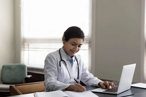 사무실에서 노트북을 사용하여 필기를 하고 있는 인도 여성 의사를 가르치는 모습 — 스톡 사진