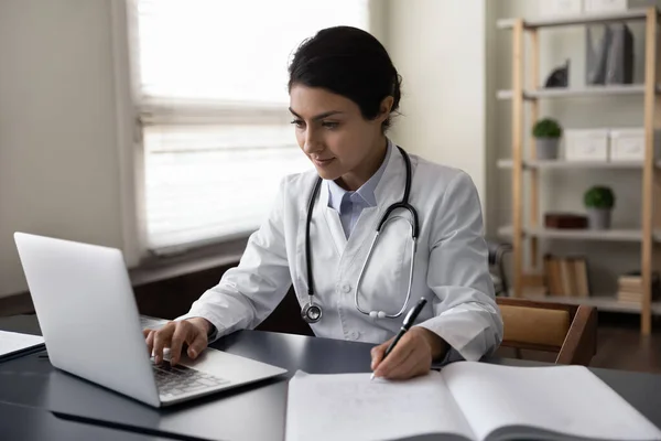 Allvarlig indisk kvinnlig läkare som använder laptop, anteckna — Stockfoto