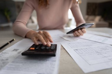 Hesap makinesi ve akıllı telefon kullanarak faturaları hesaplayan kadını kapat