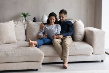 Oturma odasındaki kanepede dijital tabletle dinlenen çift.