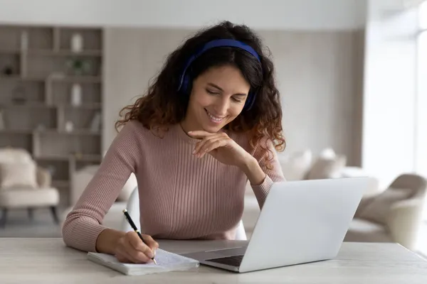 Foto de la cabeza sonriente mujer en auriculares tomando notas viendo webinar — Foto de Stock