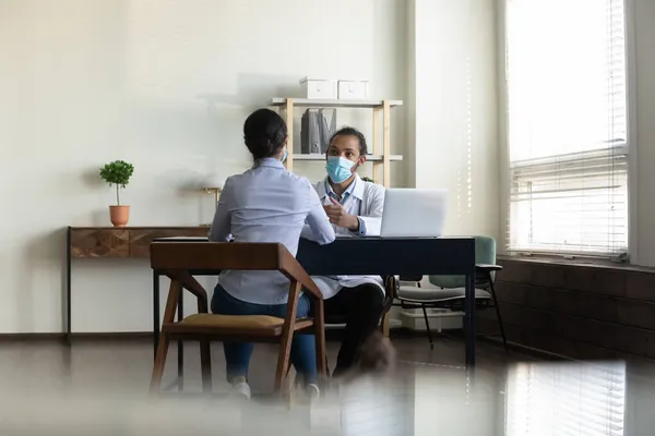 Rear view African American doctor in mask consulting Indian woman — Stock Photo, Image