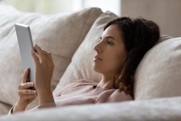 Cerca de la mujer usando el dispositivo de la tableta, relajándose en el sofá — Foto de Stock