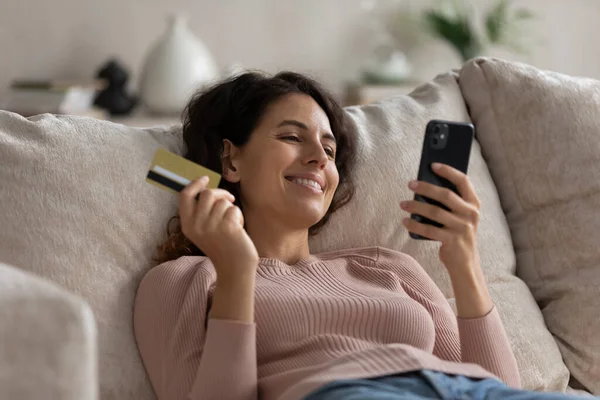 Blisko uśmiechnięta kobieta trzyma złotą kartę kredytową i smartfona — Zdjęcie stockowe