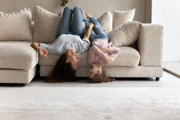 Happy mother and little daughter lying upside down on couch