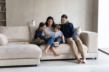 Çocuklu bir çift kanepeye oturur ve büyüleyici bir masal kitabının tadını çıkarır.