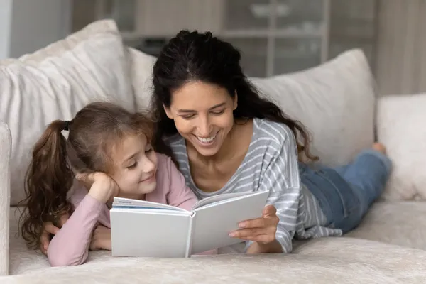 De cerca madre cariñosa con linda hija leyendo libro juntos —  Fotos de Stock