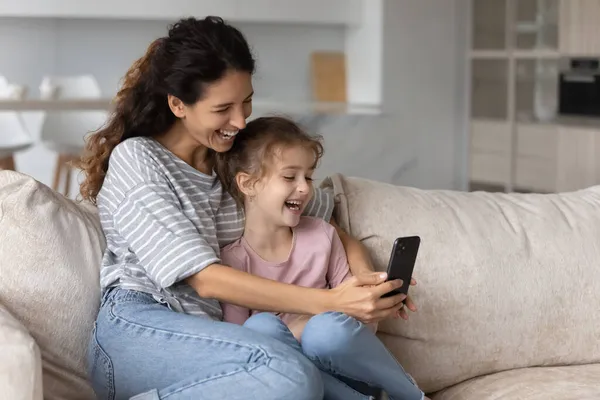 Madre llena de alegría con linda hija chica divirtiéndose con el teléfono inteligente — Foto de Stock