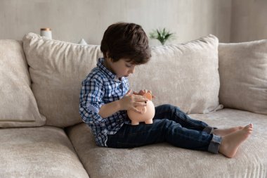 Anaokulu çocuğu kanepeye otur ve kumbaraya bozuk para at.