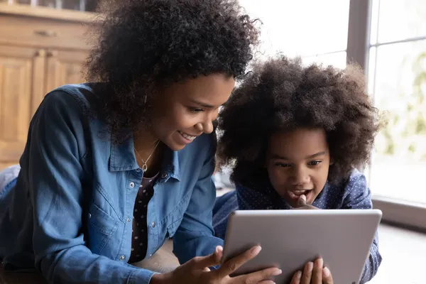 Cuidado sonriente joven afroamericana madre usando tableta con niño. — Foto de Stock