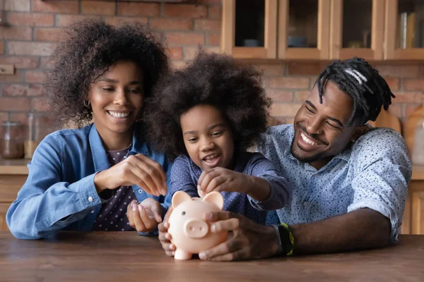 Cuidar de jovens pais afro-americanos ensinando a filha pequena economizando dinheiro, — Fotografia de Stock