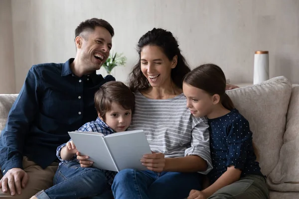 Família alegre com crianças sentar no sofá lendo um livro — Fotografia de Stock