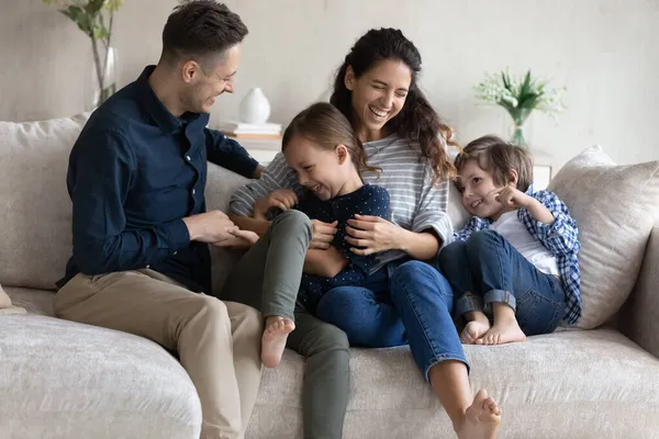 Lachendes Paar kitzelt kleine Kinder auf Sofa zu Hause — Stockfoto