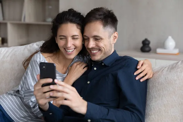 Paar sitzt auf Sofa und schaut lustige Videos auf Handy — Stockfoto