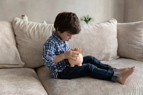 Niño preescolar sentarse en el sofá tirar monedas en alcancía —  Fotos de Stock