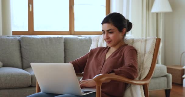 Positive young Indian woman rest in armchair use laptop — Stock Video