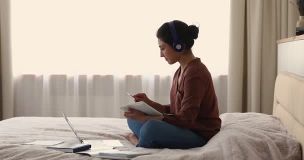 Indiai nő fülhallgatóban ül az ágyban tanulmány előtt laptop — Stock videók