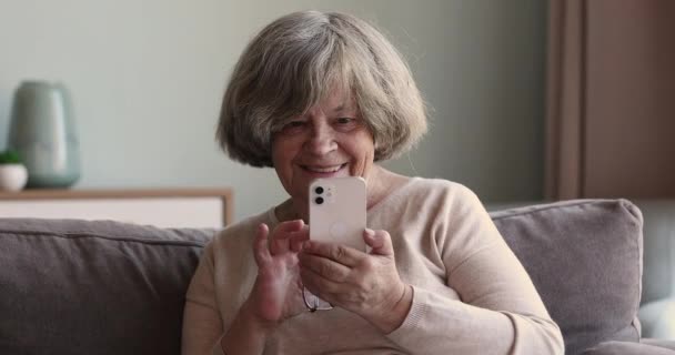 Confiada abuela mayor sentarse en el sofá utilizar el trabajo de teléfono en línea — Vídeos de Stock