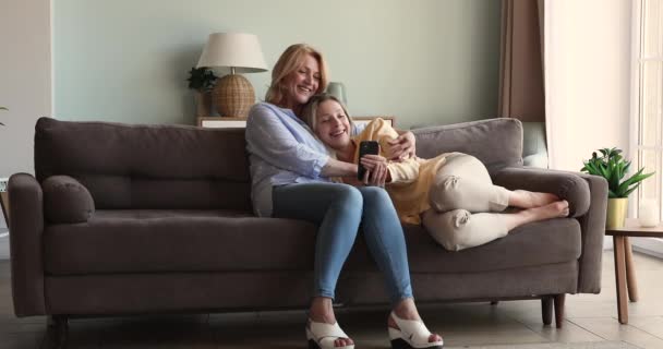 Jong dochter knuffelen naar volwassen moeder kijken video op cel — Stockvideo