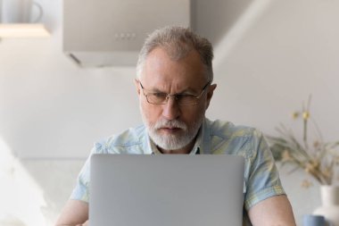 Gözlüklü, laptopta çalışan 60 'lı yaşlarda bir adam.