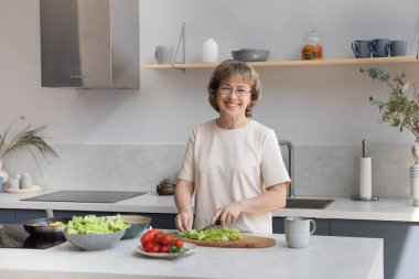 Masada salata için taze sebze doğrayan mutlu yaşlı bayan.