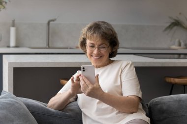 Gözlüklü neşeli yaşlı bayan mesaj okuyor.