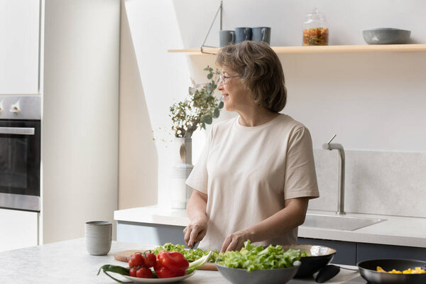 Happy mature woman making salad in kitchen