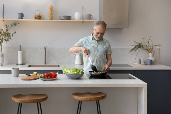 Mature 60s homeowner man cooking dinner in kitchen