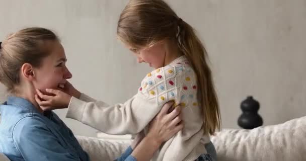 Взрослая старшая сестра и маленькая школьница щекочут на уютном диване — стоковое видео