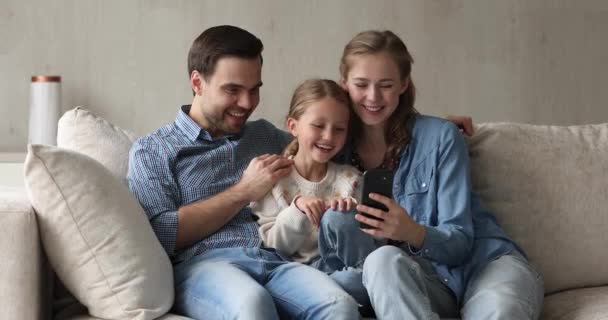 Дружелюбная мама папа маленькая дочь обнимается смотреть видео по телефону — стоковое видео