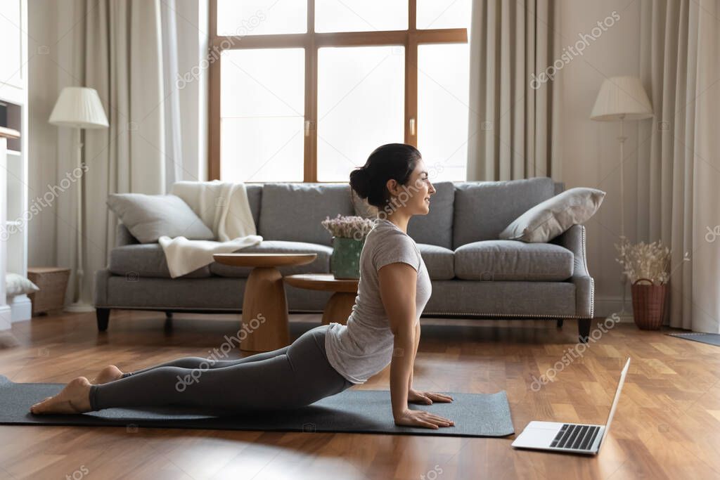 Happy young indian woman stretching muscles, enjoying online yoga class.