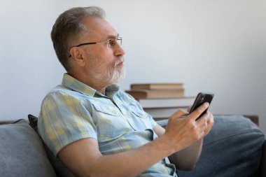 Düşünceli üst düzey cep telefonu kullanıcısı akıllı telefondan sohbet ediyor.