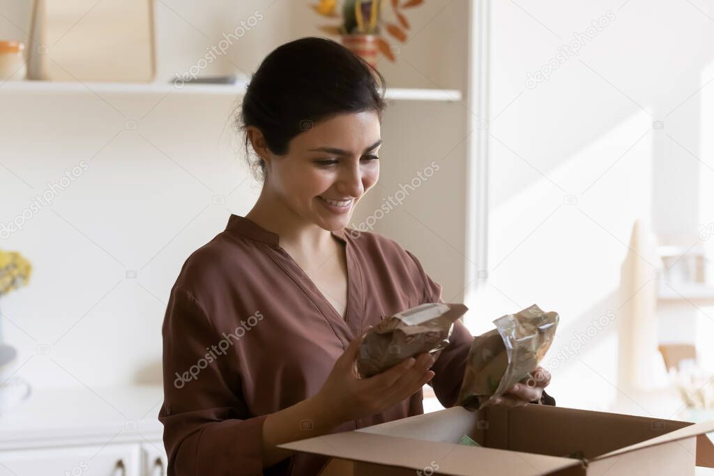Happy indian woman unpacking parcel from store with healthy food.
